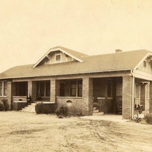 White woman sitting on steps of her single-story brick house with car in garage