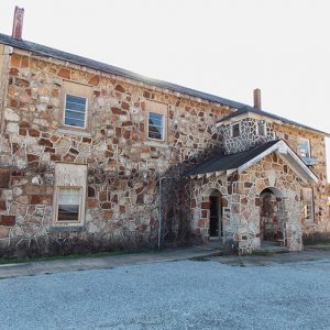 Multistory stone building with arched entry way and school buses parked beside it