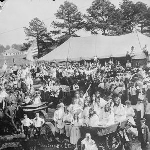 Large group of children and adults standing and seated in front of large tent