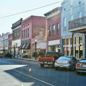 Single-story and two-story storefronts on street with parked cars