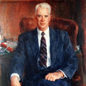 White man with in suit and tie sitting at his desk