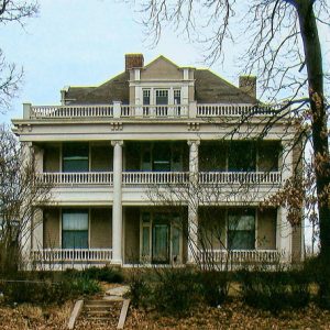 Multistory house with covered porch and balconies on sidewalk with steps under bald trees