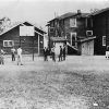 young African-American men playing basketball outside with school buildings in the background and young African American women watching