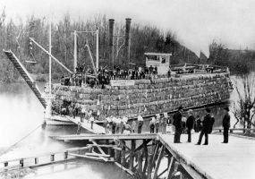 Passengers boarding a steamboat loaded with cotton bales
