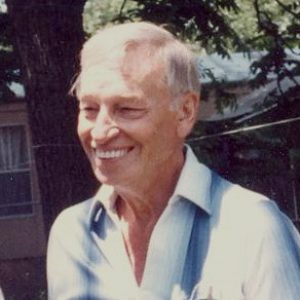 Older white man smiling in collared shirt with house and tree behind him