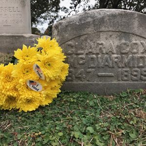 Yellow flowers with "I Voted" stickers next to small gravestone in cemetery