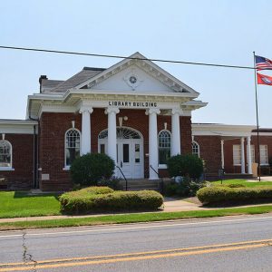 Brick library building with two wings and porch supported by four columns with arched doorway on street