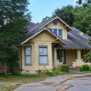 Multistory house with covered porch and overgrown circular driveway