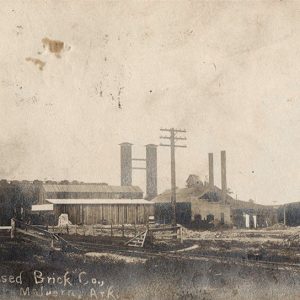 Factory buildings with smoke stacks and railroad tracks in the foreground