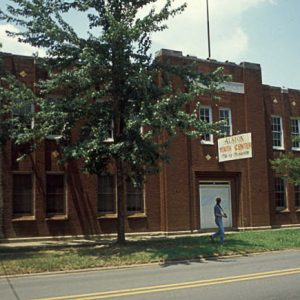 Two-story brick building with trees and sign above its front door