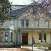 Three-story pale yellow house with green trim ornate porch and balcony above porch