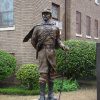 Bronze statue of white man in military uniform with sword in front of brick building