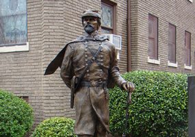 Bronze statue of white man in military uniform with sword in front of brick building