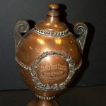 Copper urn with inscription and wreath detail on shelf