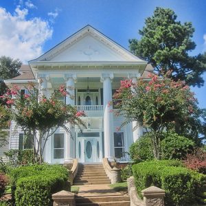 Front view of multistory house with covered porch and four columns with trees around it