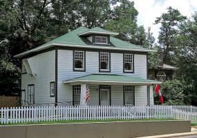 Multistory house with covered porch inside white picket fence