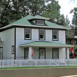 Multistory house with covered porch inside white picket fence