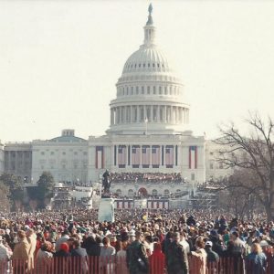 Massive crowd in front of multistory marble building with large dome with flags and banners hanging below it