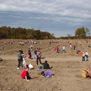 Crowd of tourists digging in dirt field for diamonds