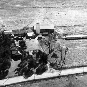 Dairy factory buildings and trees on farmland with two-lane road in the foreground as seen from above