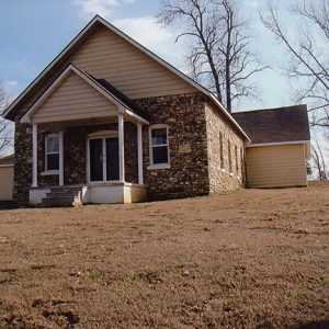 Single-story house with covered porch and stone walls on hill