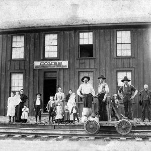 White adults and children pose with handcar outside wood frame "combs" train station