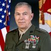 White man in military uniform featuring medals with flags beside him