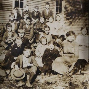 Group of white children and white woman outside school house