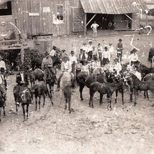 White men and horses with farm buildings around them