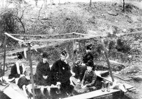 Women in hats and dresses sitting around a hot spring