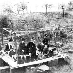 Women in hats and dresses sitting around a hot spring