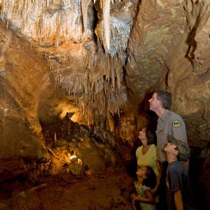 White park ranger and white woman and children marveling inside a deep cave with stalactites hanging from above