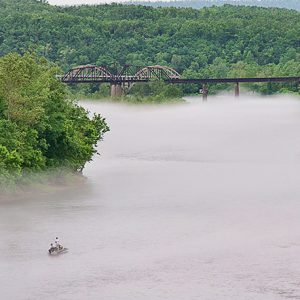 Steel truss bridge over river with tree-covered countryside in the background