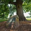 Stone marker with information plaques under a tree in an area lined with small wrought-iron fence