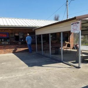 White man at brick building with chairs and tables under metal pavilion