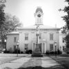 Symmetrical building with clock tower located behind stone monument with lamps on either side of it