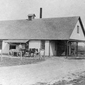 Man and horse-drawn wagon outside single-story building with covered entrance