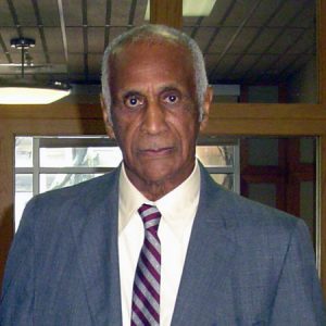 older black man with serious expression and short white hair and sideburns in suit jacket and striped tie