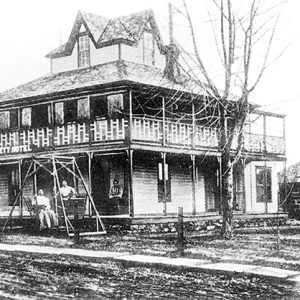 Two-story hotel with tower room on dirt road and tree