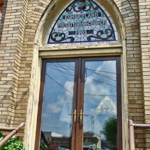 Close-up of blond brick building with stained glass window above double glass doors