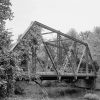 Steel truss bridge partially covered with ivy and concrete platform