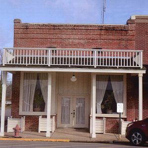 Red car parked outside brick storefront with covered entrance and balcony