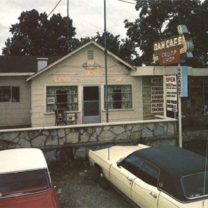 Cars parked outside "Dam Cafe" building with neon sign