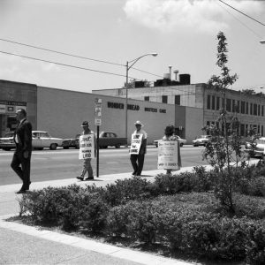 White men with protest signs on city sidewalk outside "Wonder Bread Hostess Cake" building