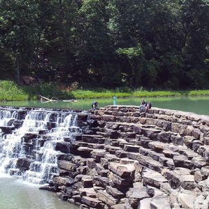 Three people sitting on dam with water overflowing