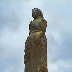 Statue of woman on grave marker with blue sky