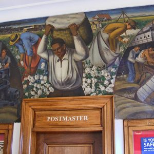 Multicolored painting of workers in factory on a cotton field and loading boats on dock hanging in post office