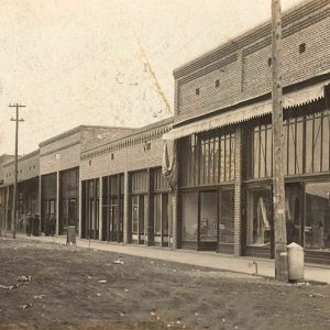 "Harmon's" store with display windows and brick storefront buildings on dirt street