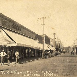 Townspeople and horse drawn wagons on town street lined with storefronts