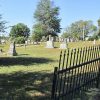 Gravestones in cemetery with black iron fence and trees